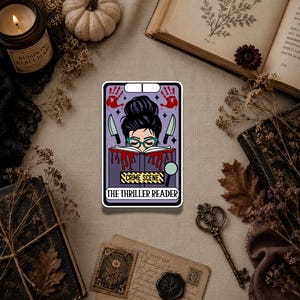 May include: A rectangular sticker featuring a purple tarot card design with a person reading a book. The illustration includes red handprints, two knives, a magnifying glass, and yellow caution tape with the text CRIME SCENE and THE THRILLER READER.