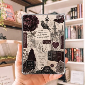 May include: A rectangular tablet case featuring a dark aesthetic collage with a large peony, a raven, a key, a castle, a moth, a hooded figure, and books. Text includes: I am not afraid of the darkness. It is where I've learned to light my own fire.