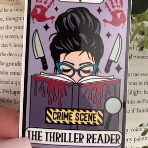 May include: A rectangular sticker featuring a tarot card design with a purple background. It shows a person with a dark bun and teal glasses reading a book with red liquid dripping from it. Two knives, two red handprints, and a magnifying glass are visible.