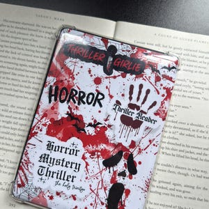 May include: A white and red horror-themed phone case with the words "Thriller Girlie", "Horror", "Thriller Reader", and "Horror Mystery Thriller" printed on it. The case has a blood splatter design and bat and handprint graphics.