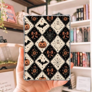 May include: A rectangular tablet case featuring a repeating diamond pattern in black and cream. The design includes illustrations of orange jack-o'-lanterns, white ghosts, black bats, spiderwebs, and brown bows, accented with small stars and crescent moons.