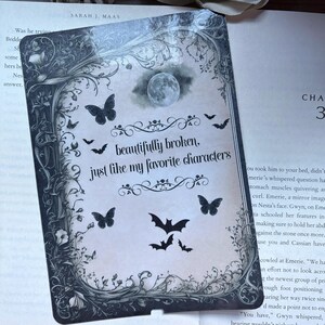 Puede incluir: Una tarjeta decorativa con estética vintage, con una luna llena, mariposas y murciélagos. La tarjeta tiene el texto "beautifully broken, just like my favorite characters" en una fuente decorativa. La tarjeta es de Sarah J. Maas.