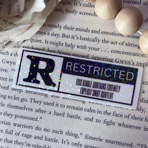 May include: A rectangular sticker with a holographic finish featuring a large black letter R on the left side. The right side contains the text RESTRICTED and THIS KINDLE CONTAINS EXTREMELY EXPLICIT SMUT CONTENT in black capital letters.