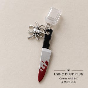 May include: A USB-C dust plug featuring a silver-toned spider charm and a miniature knife pendant with a black handle and a silver blade marked with red blood-like splatters. The text reads USB-C DUST PLUG, Comes in USB-C & Micro USB.