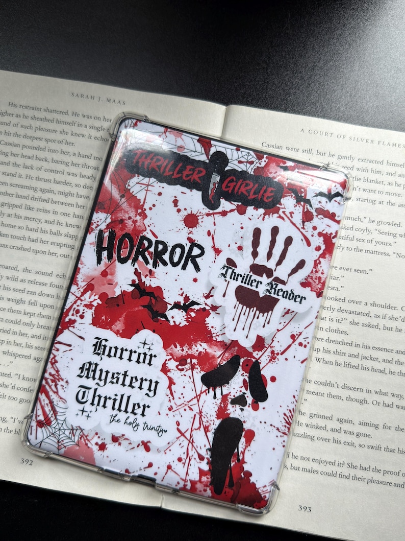 May include: A clear phone case with a white background, splattered with red paint and black accents. The case features the words "HORROR," "Thriller Girlie," and "Horror Mystery Thriller" in a spooky font. A handprint and bat silhouettes are also visible.