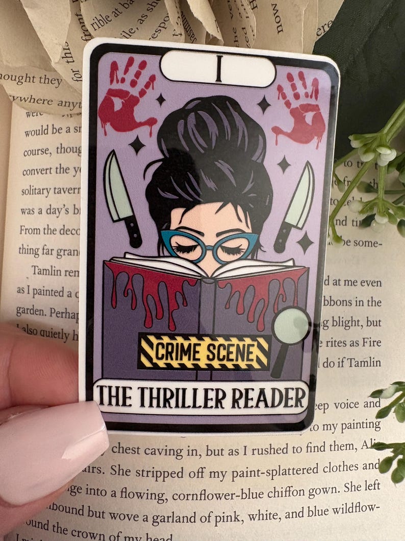 May include: A rectangular sticker featuring a tarot card design with a person in blue glasses reading a book covered in red blood drips. The sticker includes two knives, two red handprints, a magnifying glass, and the text CRIME SCENE and THE THRILLER READER.
