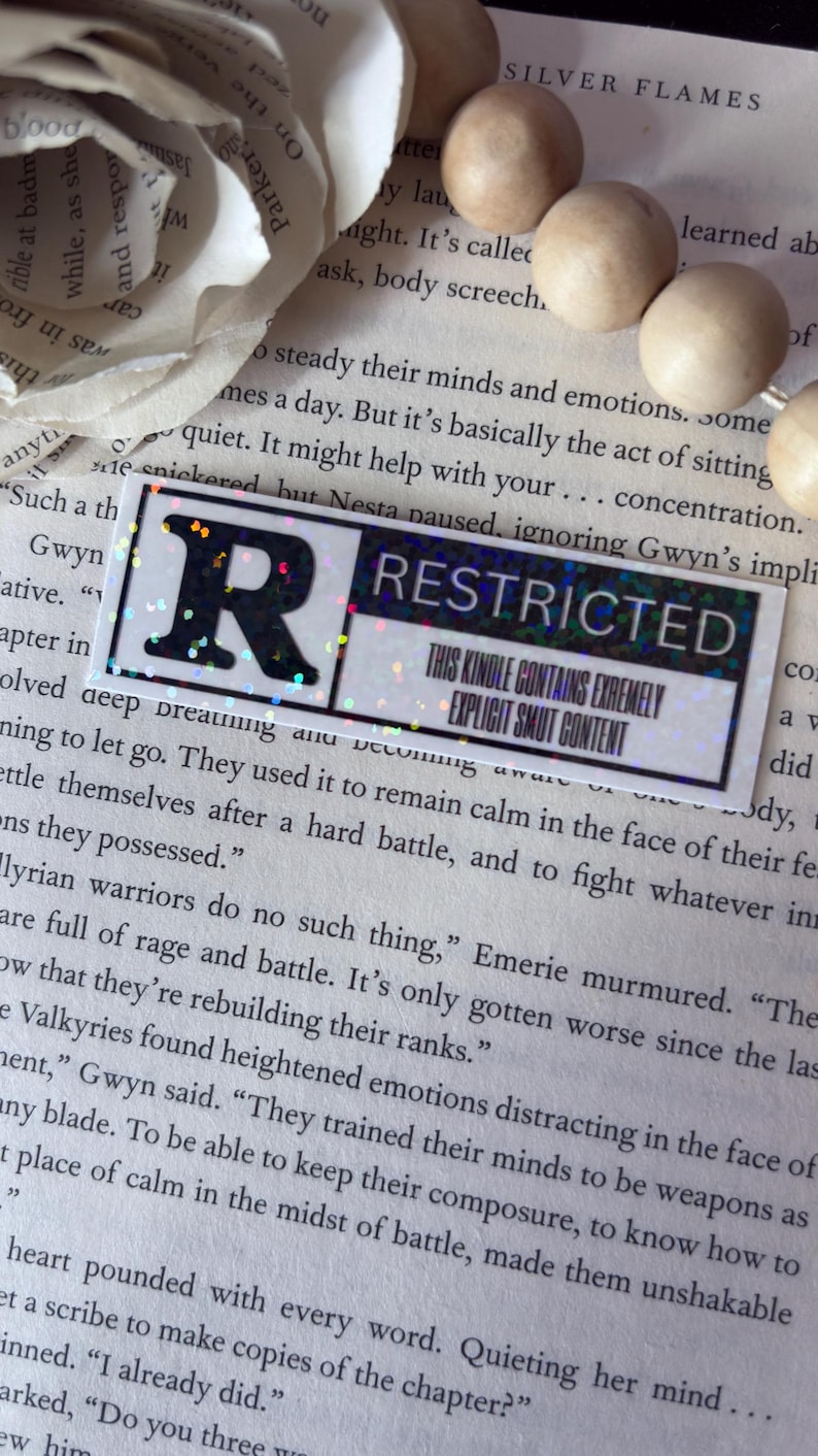 May include: A rectangular sticker with a black letter R on the left and the word RESTRICTED in black on the right. Below the word RESTRICTED, the text reads THIS KINDLE CONTAINS EXTREMELY EXPLICIT SMUT CONTENT. The sticker has a holographic finish.
