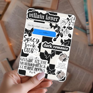 May include: A phone case with a black and white checkered pattern and various stickers. The stickers include text like "villain lover," "Spicy book club," and "dark romance." Other stickers feature bats, roses, and a skull with a knife.