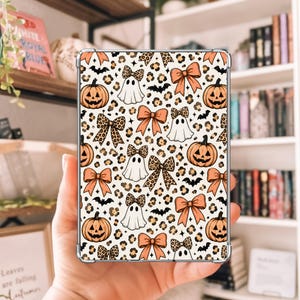 May include: A clear tablet case featuring a repeating pattern of orange jack-o'-lanterns, white ghosts, solid orange bows, and leopard print bows against a cream background with small black bats and stars scattered throughout the design.