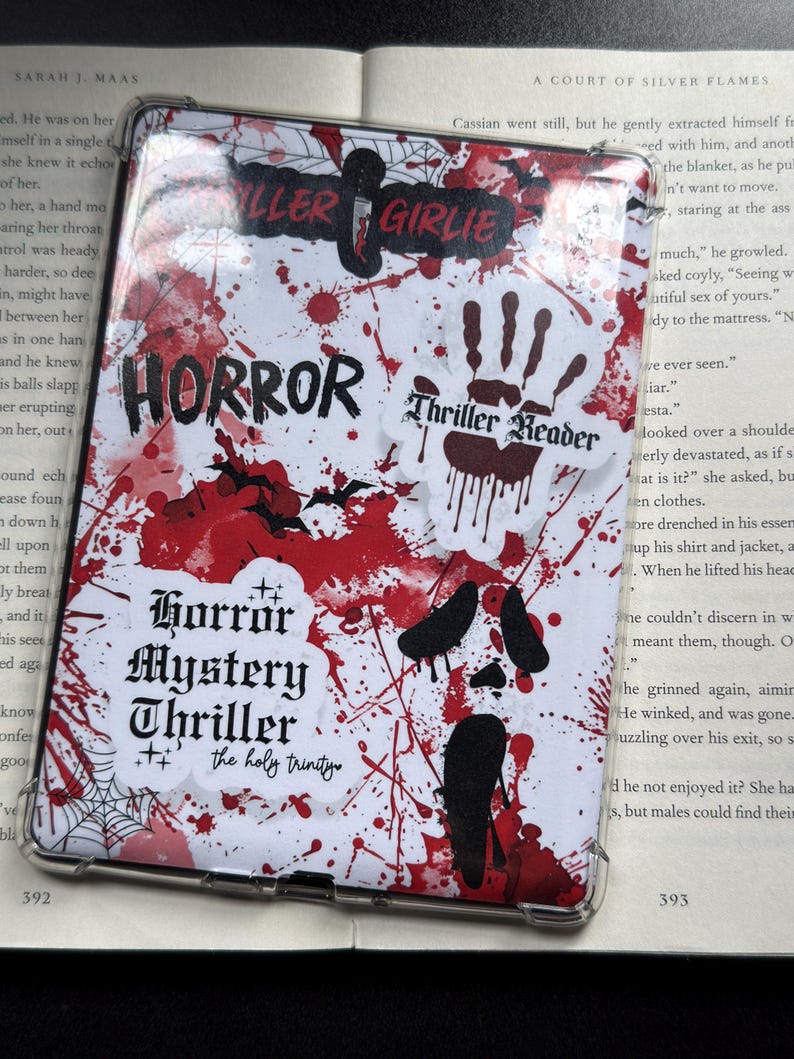 May include: A clear protective case for an e-reader, featuring a horror-themed design. The case is white with red blood splatter and various stickers with text like "HORROR" and "Thriller Reader".