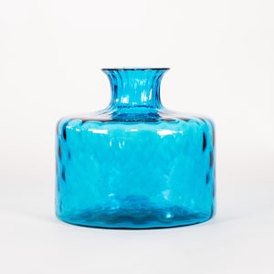May include: A vibrant turquoise glass vase with a textured, diamond-like pattern. The vase has a wide, rounded body and a flared, ruffled neck. The clear glass allows light to pass through, creating a beautiful display.