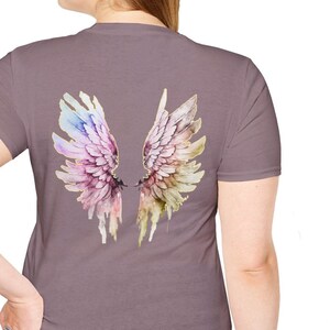 May include: A mauve t-shirt with a watercolor design of a pair of angel wings on the back. The wings are a mix of pink, purple, and yellow.