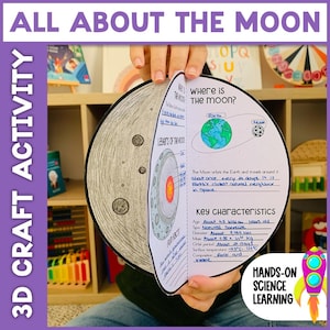 May include: A 3D craft activity book titled "All About The Moon" is held open, showing illustrations of the moon's layers and key characteristics. The book includes text and diagrams about the moon's orbit and features. The words "Hands-On Science Learning" are also visible.