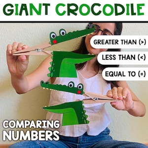 Può includere: Supporto visivo educativo con ritagli di coccodrilli verdi attaccati a mollette di legno, che illustrano il confronto di numeri. Il testo include "GIANT CROCODILE", "COMPARING NUMBERS", "GREATER THAN (>)", "LESS THAN (<)" e "EQUAL TO (=)".