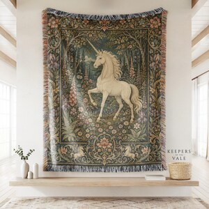 May include: A woven tapestry throw blanket featuring a central white unicorn standing in a lush forest with colourful flowers and foliage. The border displays intricate floral patterns and two smaller unicorns. Text reads Keepers of the Vale.