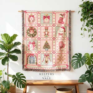 May include: A woven throw blanket featuring a grid of twelve festive Christmas-themed squares in shades of pink, cream, and green. The pattern includes illustrations of ornaments, a perfume bottle, a stocking, a wreath, a nutcracker, a cat, a gift, a tree, a mitten, a window, a ballet slipper, and a star.