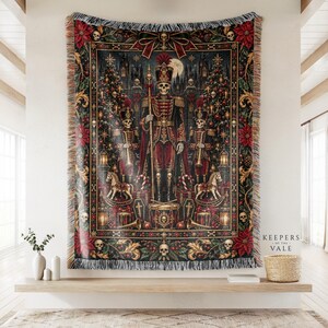 May include: A woven throw blanket featuring a dark, gothic-inspired holiday scene with a central skeleton nutcracker figure, two smaller skeleton soldiers, Christmas trees, rocking horses, and skulls, all framed by a decorative red and gold border.
