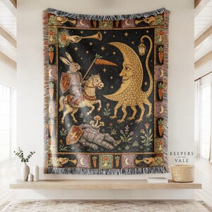 May include: A woven tapestry blanket featuring a dark background with a rabbit knight on horseback holding a carrot lance, a crescent moon creature with a lantern, and a fallen knight with mushrooms, framed by a border of carrots and moons.
