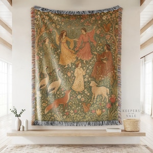 Pode incluir: Uma manta de tapeçaria tecida apresentando uma cena de floresta com figuras em mantos fluidos, uma criança usando uma coroa, dois grous, uma raposa, um cordeiro e um esquilo entre flores e árvores. As bordas têm uma franja multicolorida.