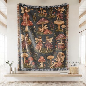 May include: A woven throw blanket featuring a dark background with a repeating pattern of fairies, mushrooms, and foliage. The fairies have wings and wear dresses, while the mushrooms vary in size and colour. The blanket has fringed edges.