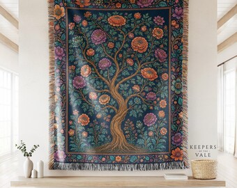May include: A woven throw blanket featuring a central tree with a twisted trunk and branches adorned with orange, purple, and teal flowers against a dark blue background. The blanket has a decorative floral border and fringed edges on all sides.