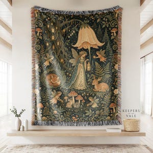 May include: A woven throw blanket featuring a dark forest scene with fairies, a fox, a deer, rabbits, and mushrooms under a large bell-shaped flower. The design includes a tree with glowing windows and the text Keepers of the Vale in the corner.