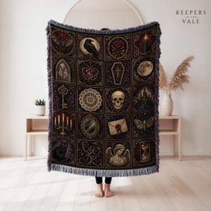 Könnte beinhalten: Eine gewebte Wohndecke mit einem Raster aus sechzehn düsteren Illustrationen, darunter ein Rabe, ein Totenkopf, eine Rose, ein Sarg, eine Motte und eine Kerze. Die Decke hat einen Fransenrand und zeigt verschiedene gotische Motive in dunklen Violett- und Goldtönen.
