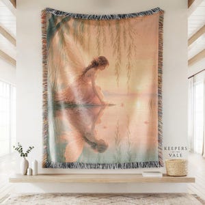May include: A woven throw blanket featuring a fairy with wings kneeling by a lake at sunset, with a reflection visible in the water. The scene includes willow branches and tall grasses. The text Keepers of the Vale is printed in the bottom right corner.