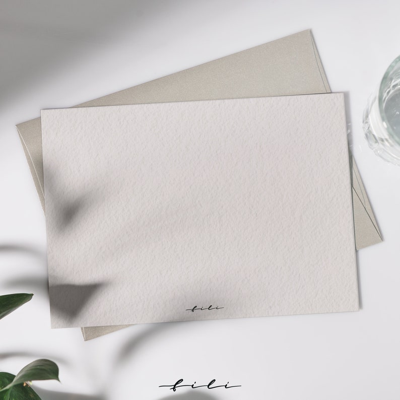 May include: A blank white card with a subtle textured surface. The card is sitting on top of a light brown envelope. The word "fili" is written in black ink at the bottom of the card.