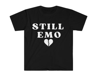 May include: Black t-shirt with the white text "STILL EMO" above a broken heart graphic. The shirt is made of a soft material and has short sleeves and a crew neck.