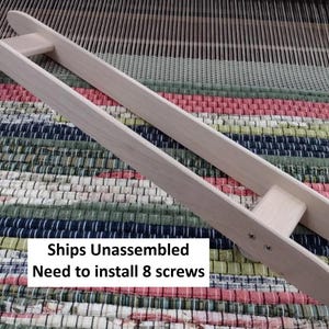 May include: A light-colored wooden weaving shuttle featuring two long, parallel side rails connected by two crossbars. The structure is held together by visible metal screws at the ends. The text "Ships Unassembled Need to install 8 screws" is printed on the image.