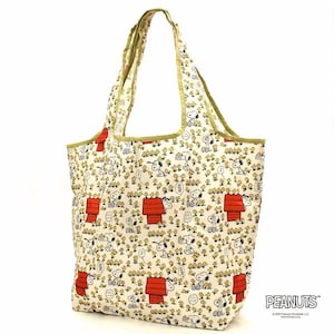 May include: A cream-colored tote bag featuring an all-over print of Snoopy and Woodstock characters, including red doghouses and small yellow birds. The bag has two shoulder straps with olive green trim along the edges and the top opening.