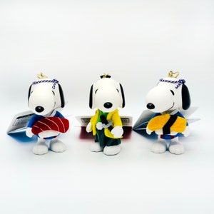 Pu&ograve; includere: Tre piccole figurine di cani di cartoni animati bianche che indossano abiti giapponesi tradizionali. Il cane a sinistra indossa un abito blu e rosso, il cane al centro indossa un abito giallo e verde e il cane a destra indossa un abito blu e giallo.