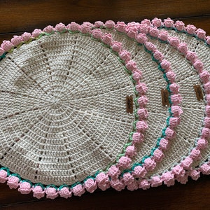 May include: Four crocheted placemats with pink and green trim. Each placemat has a small tag with the word "Stella" written on it.