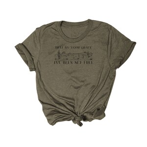 May include: A green t-shirt with a graphic of a desert landscape and the text "That by your grace I've been set free".