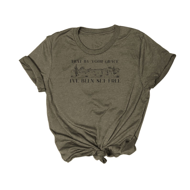 May include: A green t-shirt with a graphic of a desert landscape and the text "That by your grace I've been set free".