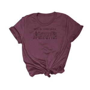 May include: A maroon t-shirt with a graphic of a desert landscape and the text "That by your grace I've been set free".