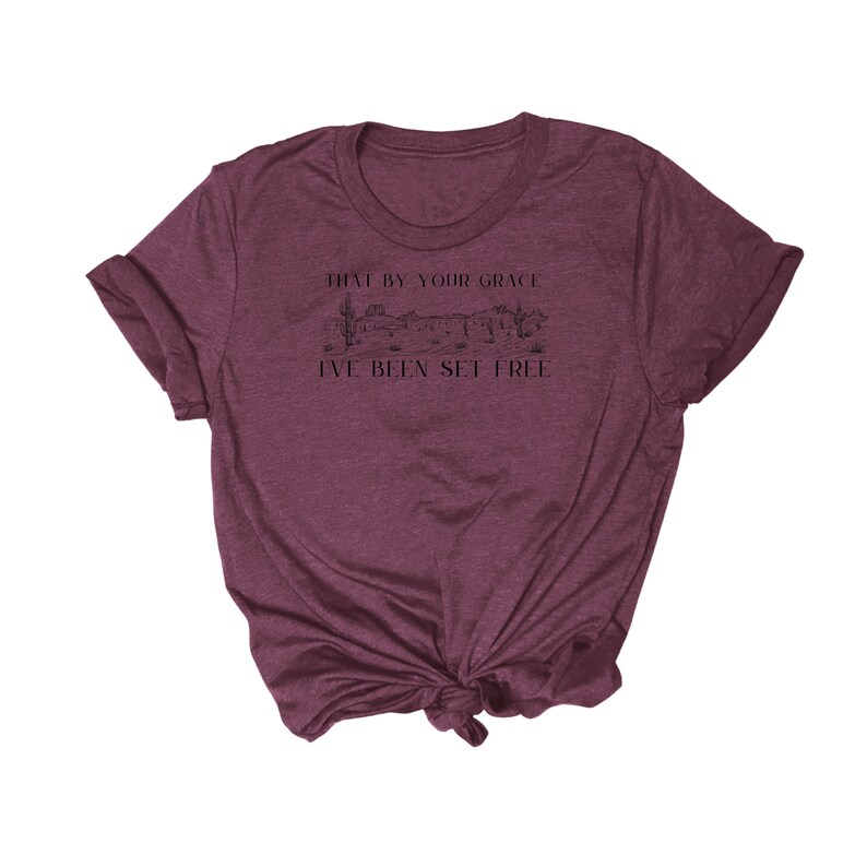 May include: A maroon t-shirt with a graphic of a desert landscape and the text "That by your grace I've been set free".