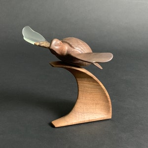 May include: A wooden sculpture of a turtle with its head up and a clear plastic fin, mounted on a wooden wave base.