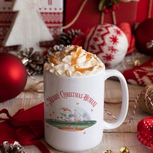 May include: White ceramic mug with a festive Christmas design featuring two cartoon aliens in a spaceship with the text "Merry Christmas Humans". The mug is filled with whipped cream and caramel sauce.
