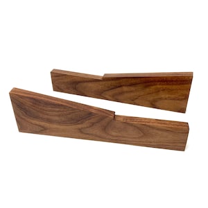 May include: Two angled wooden bookends made of dark brown wood. The bookends have a simple, modern design with a flat base and a slanted top. The wood grain is visible.