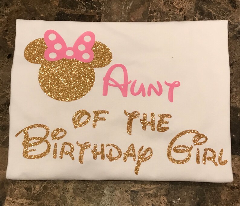 May include: White t-shirt with gold glitter Mickey Mouse ears and the text "Aunt of the Birthday Girl" in pink glitter.