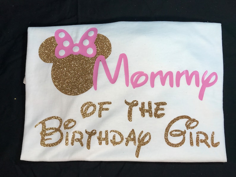 May include: White t-shirt with gold glitter lettering that says "Mommy of the Birthday Girl" and a pink glitter bow on a gold glitter Mickey Mouse head.