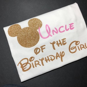 May include: White t-shirt with gold glitter Mickey Mouse ears and the text "Uncle of the Birthday Girl" in pink and gold glitter.