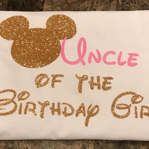 May include: White t-shirt with gold glitter Mickey Mouse ears and the text "Uncle of the Birthday Girl" in pink and gold glitter.