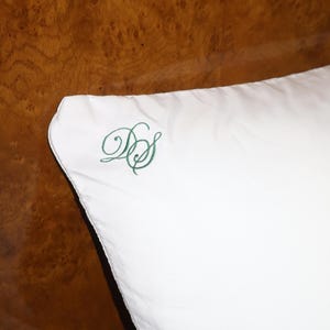 Puede incluir: Una almohada blanca con un monograma bordado en verde en la esquina. El monograma son las letras "DS" en una fuente cursiva. La almohada est&aacute; sobre un fondo de madera oscura.