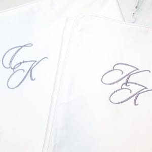 Two white pillowcases are shown, each embroidered with the intertwined gray script initials "JK".