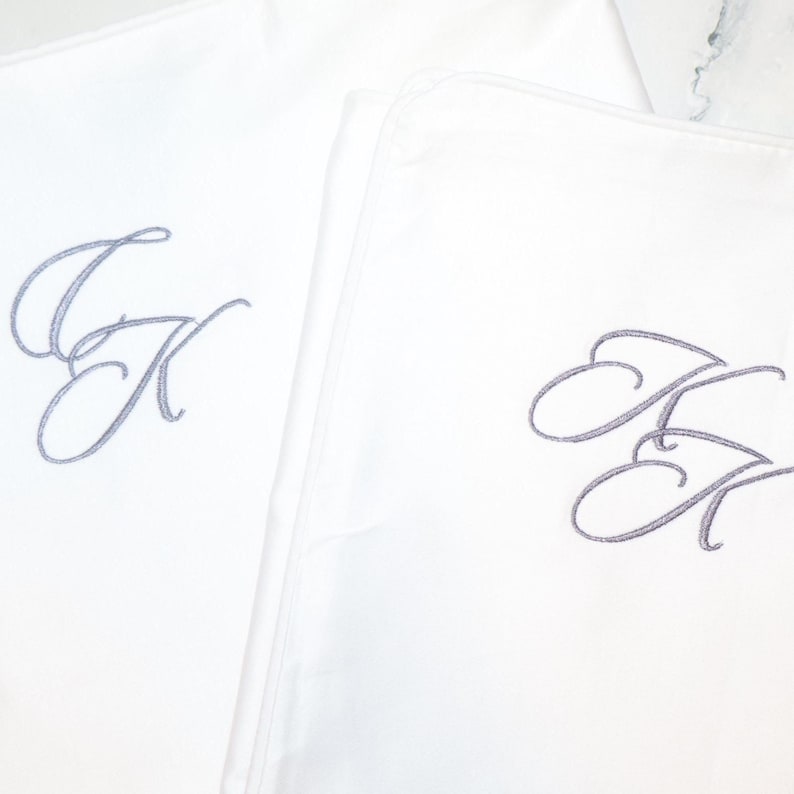 Two white pillowcases are shown, each embroidered with the intertwined gray script initials "JK".