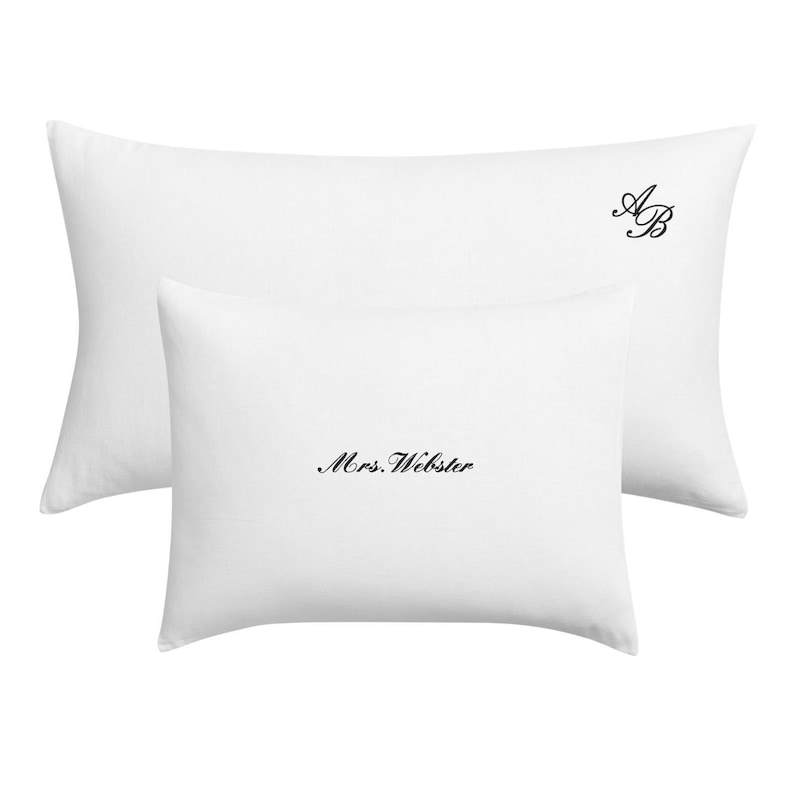Two white pillowcases, one larger than the other, with "Mrs. Webster" embroidered in script on the smaller one and "AB" in script on the larger one.