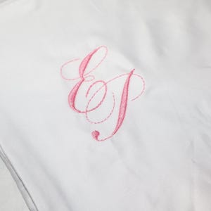 A white pillowcase is embroidered with the pink script initials "EJ".